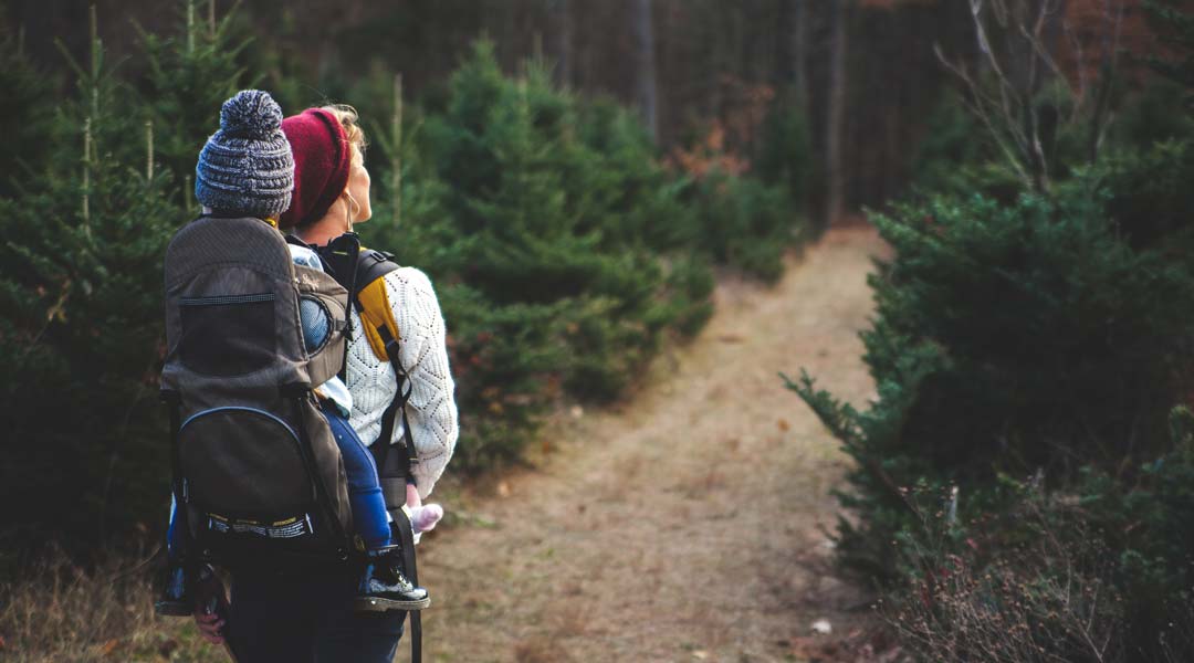Photo of a a woman carrying a child in a backpack carrier down a path in the woods